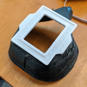 a close up of the same mask without the fabric cover and filter, the mask is made of black plastic with a white plastic frame on the front