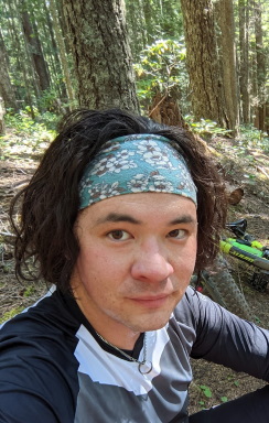 a headshot of Michael, he is male presenting with brown eyes and long hair, wearing a headband